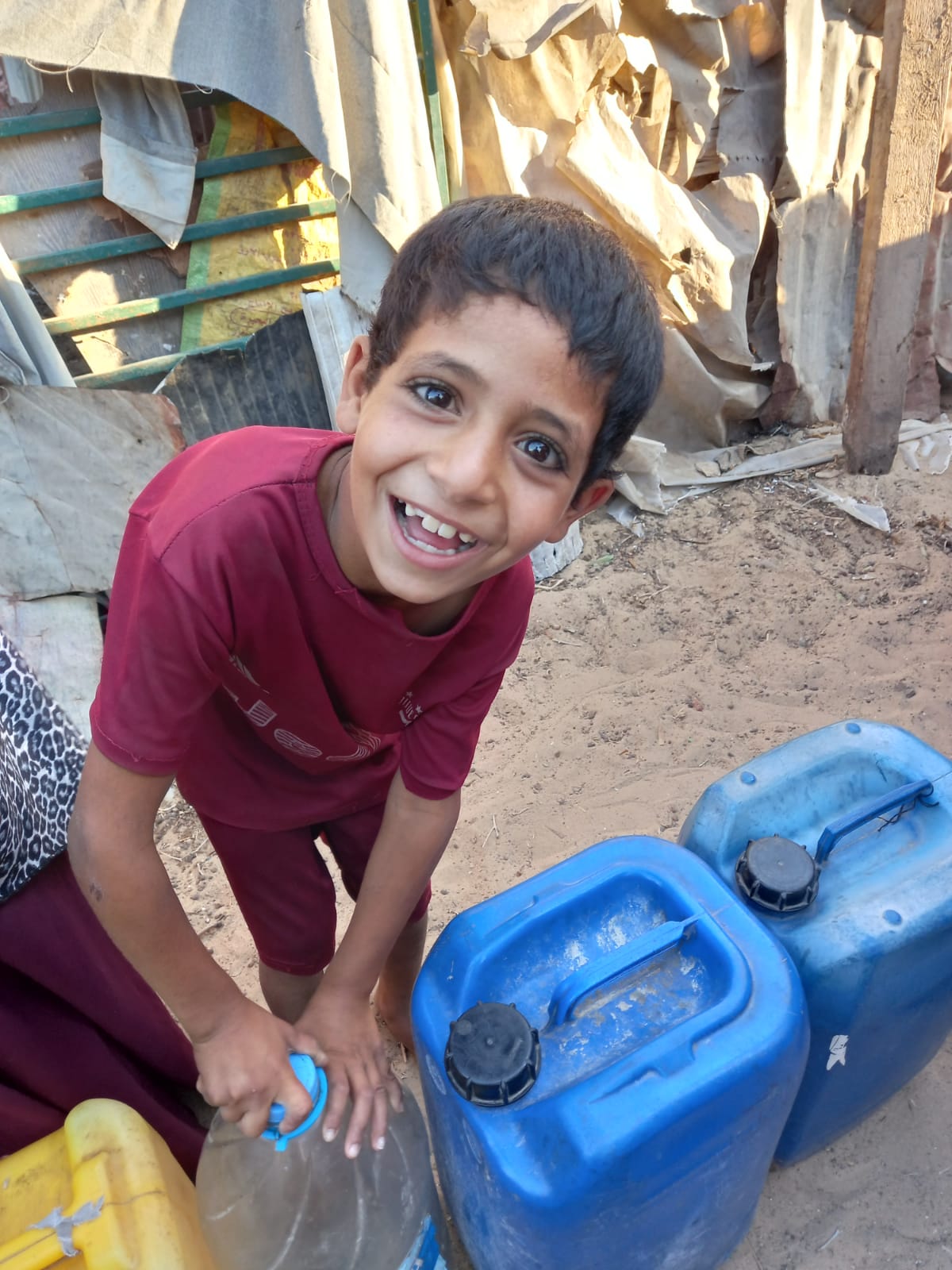 A smiling child with water containers in Gaza
